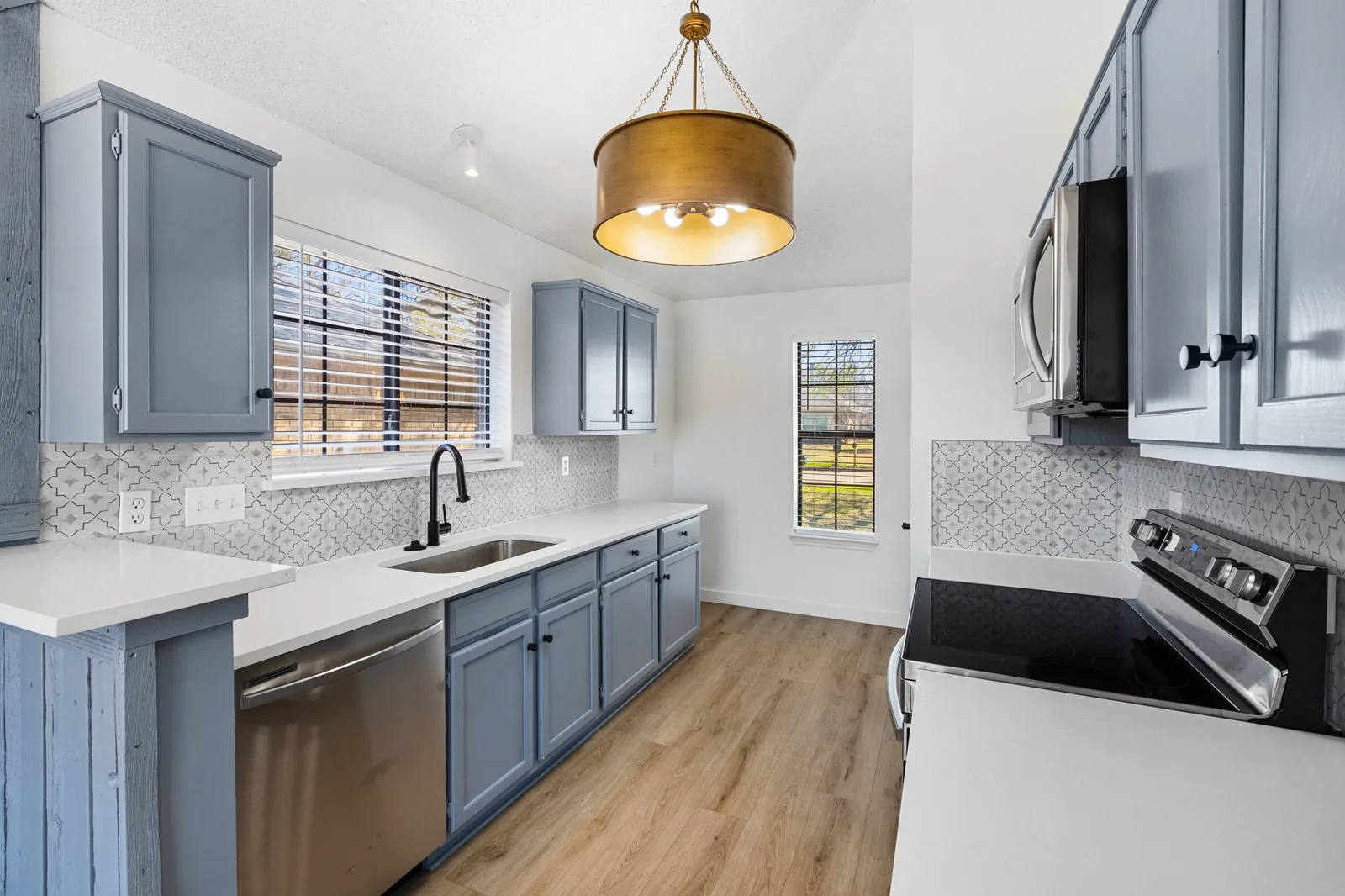 Kitchen after a pre-sale renovation at Haven Pl in Allen: painted blue-gray cabinets, white quartz counters, brass pendant, and new flooring
