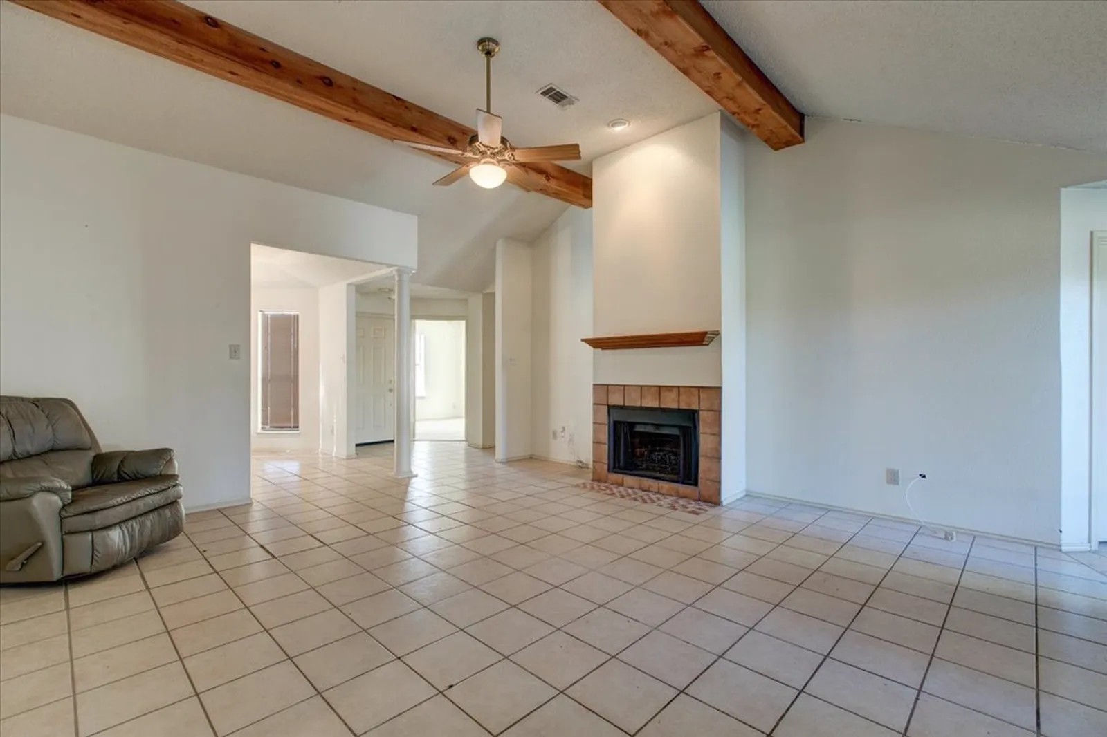 Haven Pl. living room in Allen before the renovation: beige tile floors, the original fireplace, a ceiling fan, and exposed beams