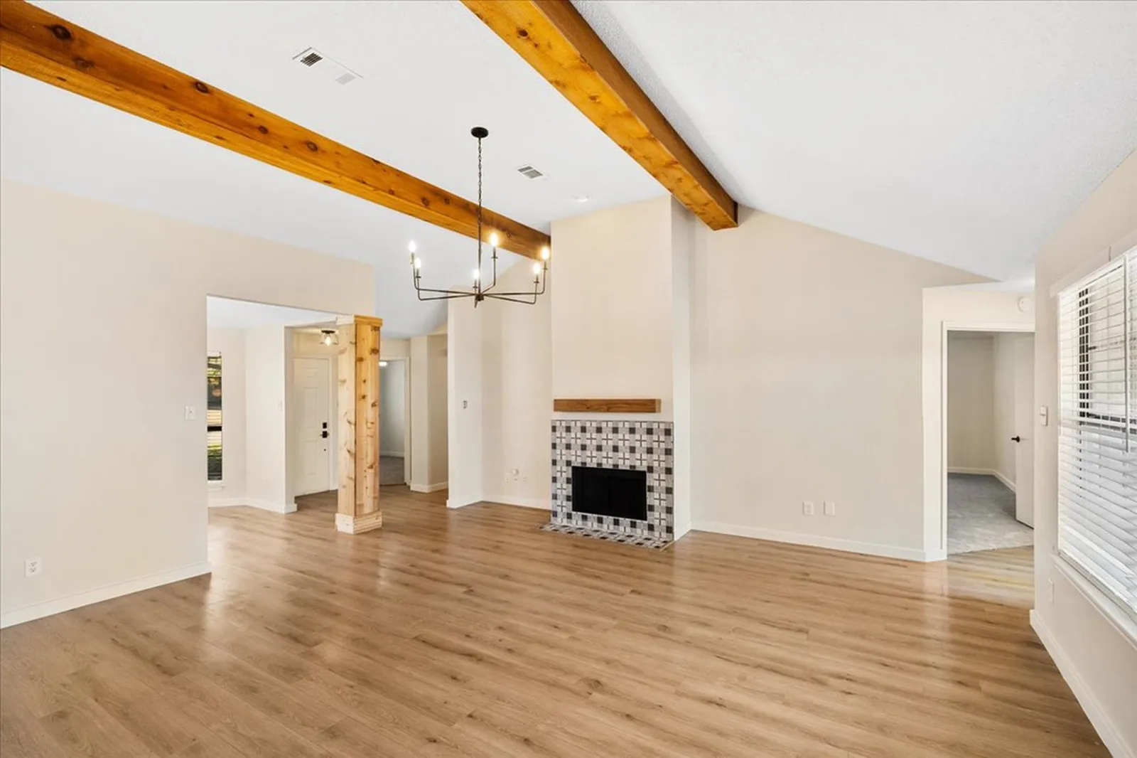 Haven Pl. living and dining area in Allen after the renovation: new plank flooring, fresh paint, a black chandelier under the exposed beams, and a patterned tile fireplace surround