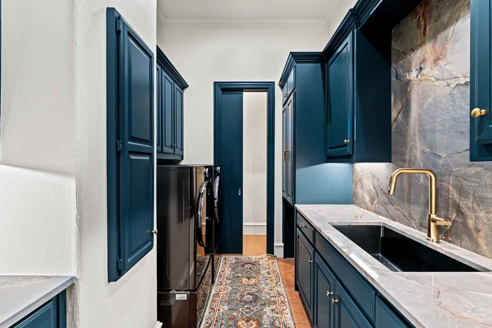 Laundry room at Prestwick Ln in Dallas: navy cabinets, quartzite backsplash, black sink, and brass faucet