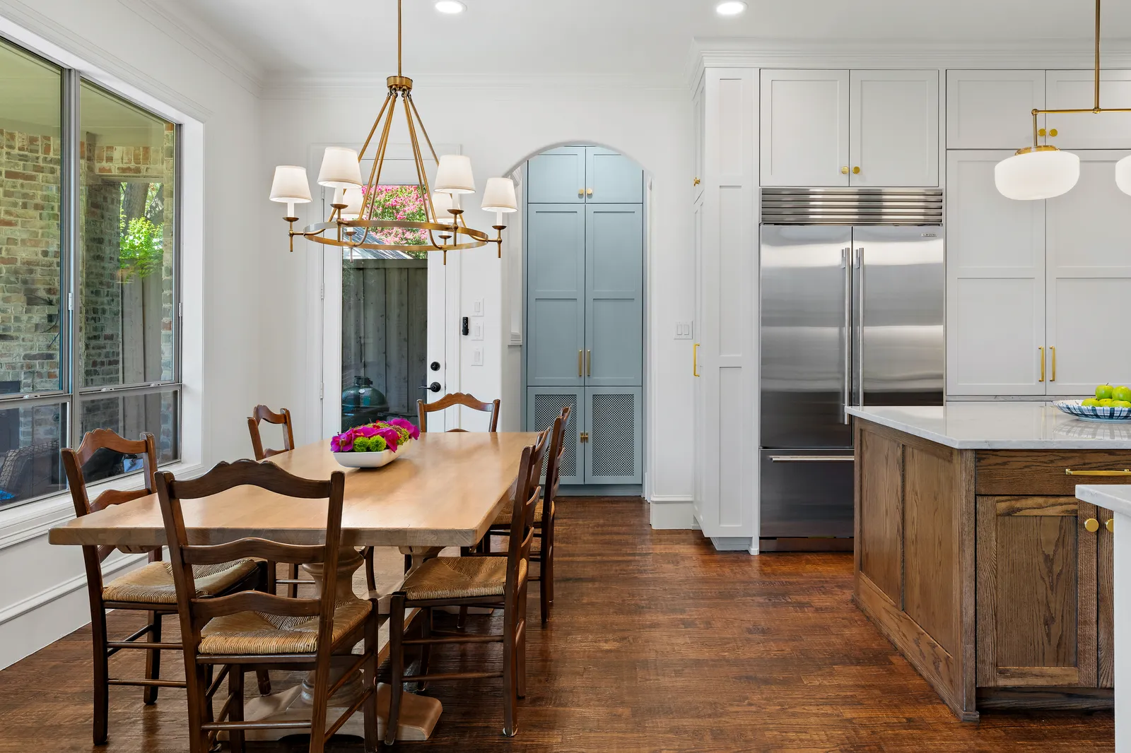 Kitchen at Revere Pl. in Lakewood, Dallas: white cabinetry, stained oak island, stone counters, brass hardware, and a light blue pantry behind an arched opening