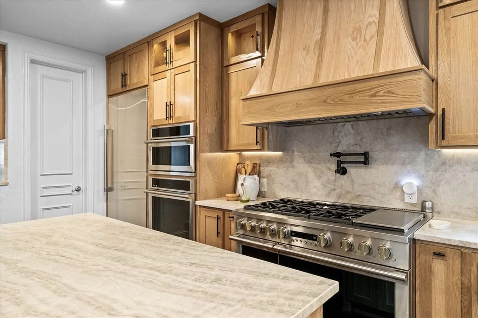 Remodeled kitchen at Shady Point Dr in Plano: white oak cabinetry, paneled refrigerator column, double ovens, white oak range hood, and a quartzite island
