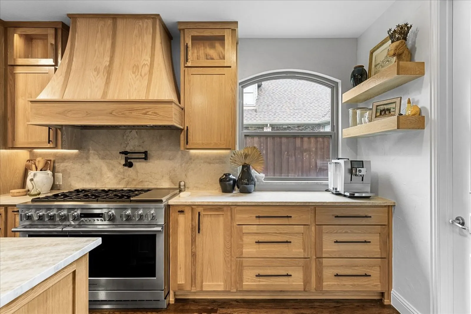 White oak range hood, pro range, quartzite backsplash, and floating shelves in the remodeled Shady Point Dr kitchen in Plano
