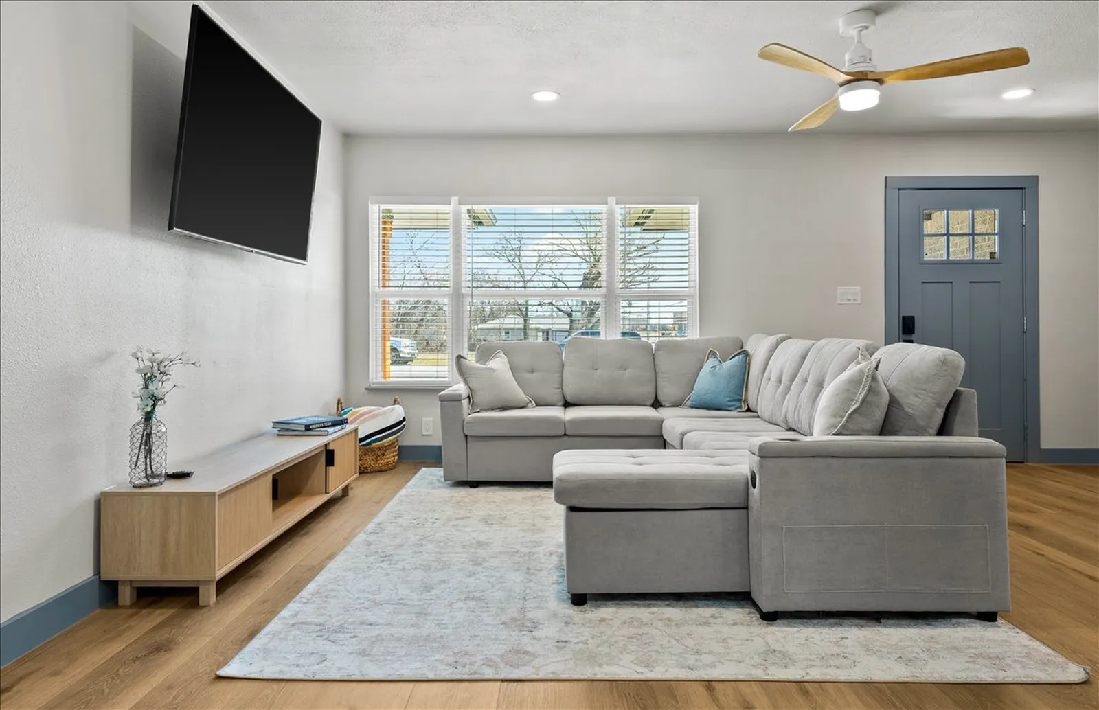 Open living room with new plank flooring and a blue front door at Sherman St. in Melissa